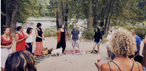 A group of people in a circle singing together at a river beach