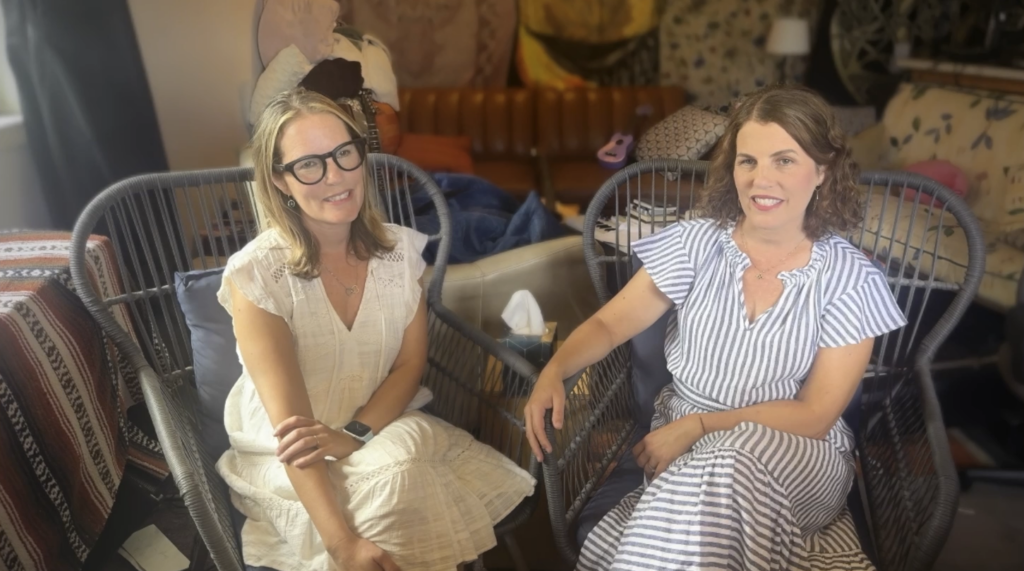 Two women seated in stylish chairs surrounded by various home decor items, smiling and engaged in conversation.